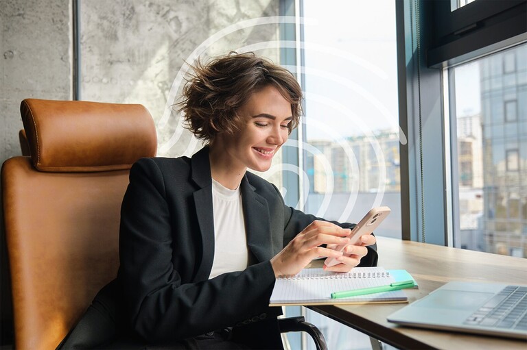 Een vrouw bekijkt haar dossier op haar smartphone aan een tafel bij het raam.