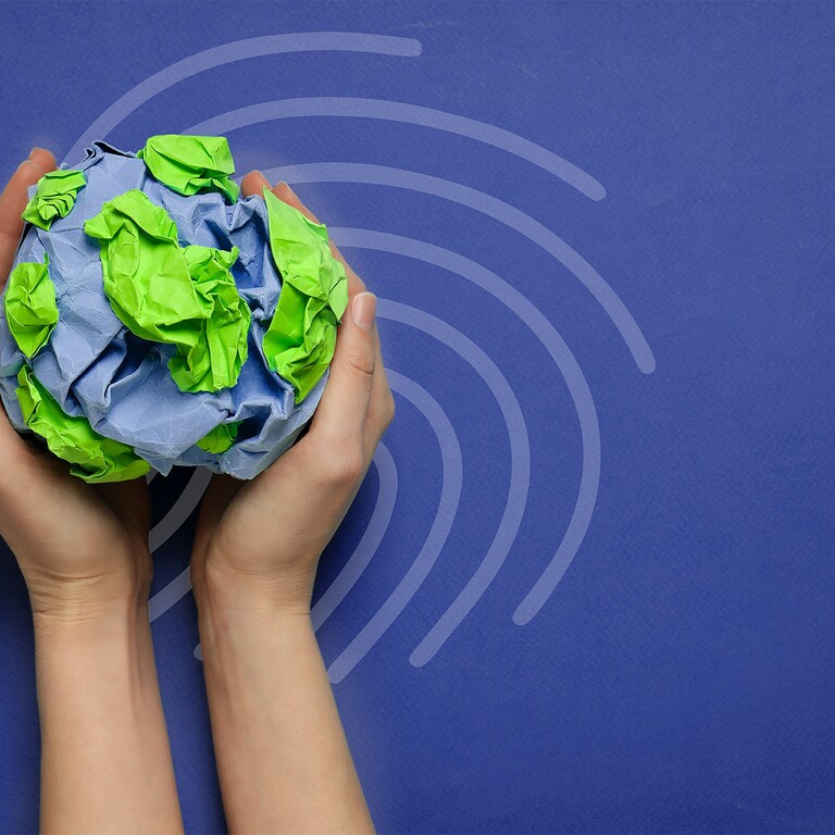 Twee handen houden een wereldbol van gekreukt blauw en groen papier omhoog.