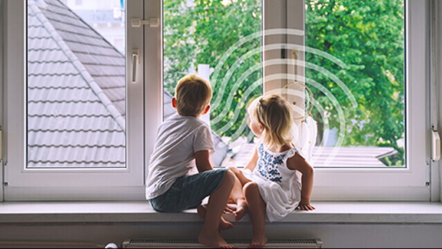 Twee kinderen zitten in een brede vensterbank en kijken naar buiten.